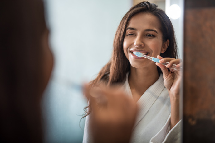 Mujer lavándose los dientes y usando flúor.
