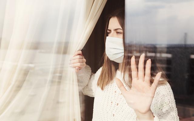 Mujer viendo desde su ventana con máscara